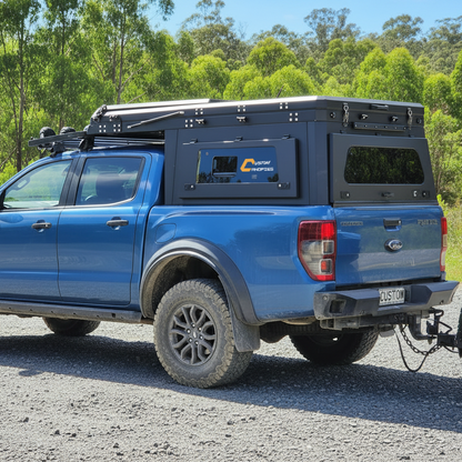 Blue truck with a camper shell on a gravel road with trees in the background